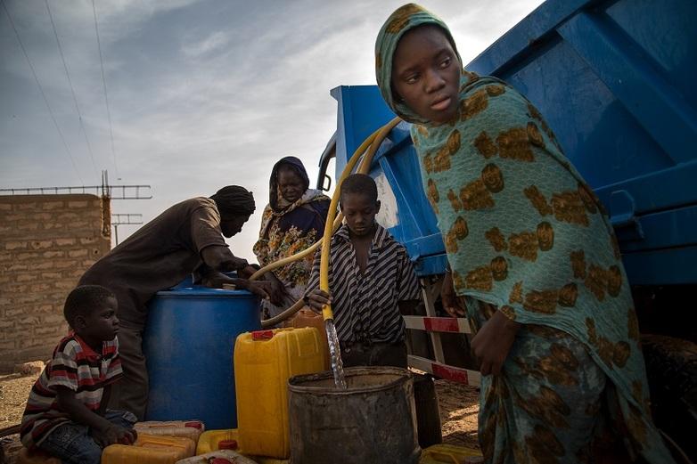 Mehrere Personen stehen neben einem Lastwagen aus dem sie über Schläuche Wasser in verschiedene Behältnisse füllen. Copyright: GIZ