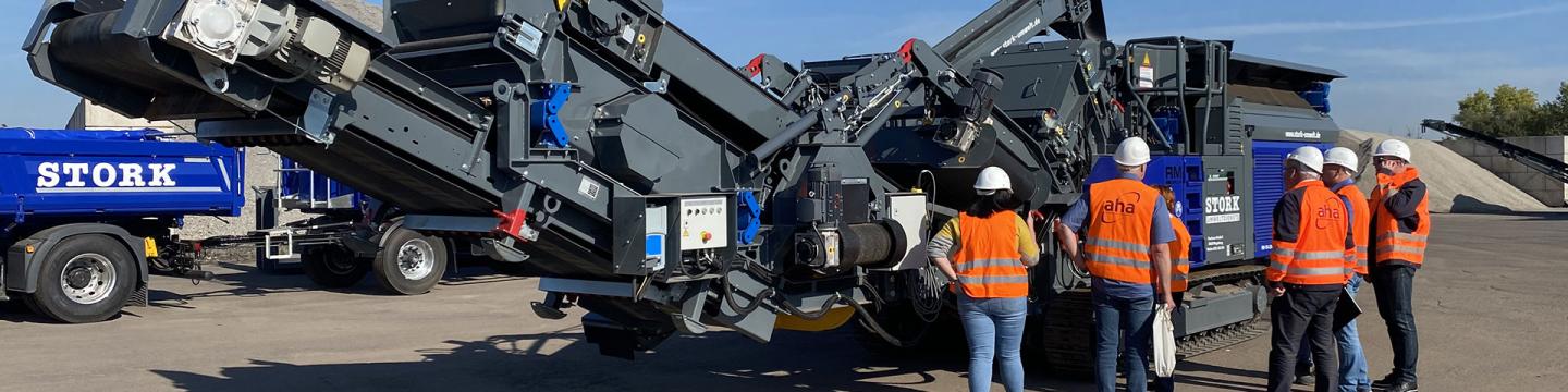 Mehrere Personen mit Warnweste stehen um eine große Baumaschine herum.