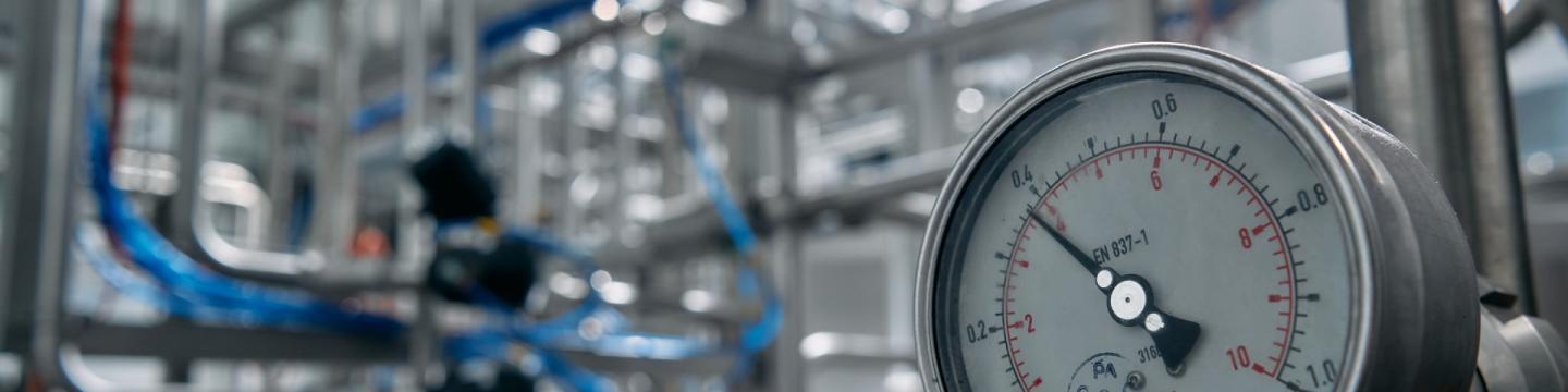 Der Fokus liegt auf der Anzeige eines Druckmessers. Im Hintergrund sind unscharf viele Rohre zu erkennen.