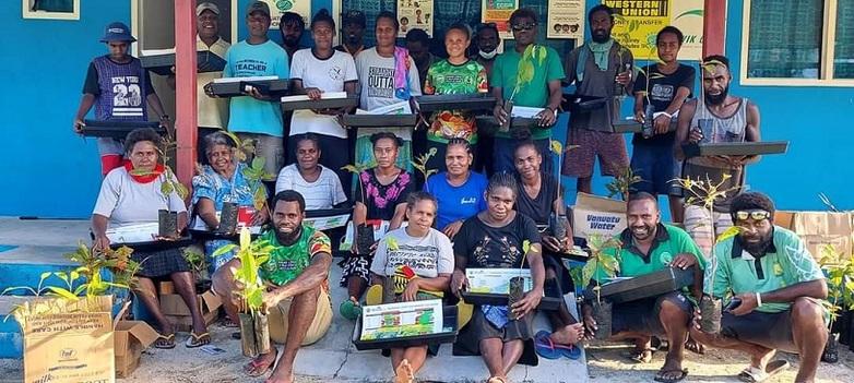 Menschen vor einer blauen Wand halten Pflanzensetzlinge und Saatgut.