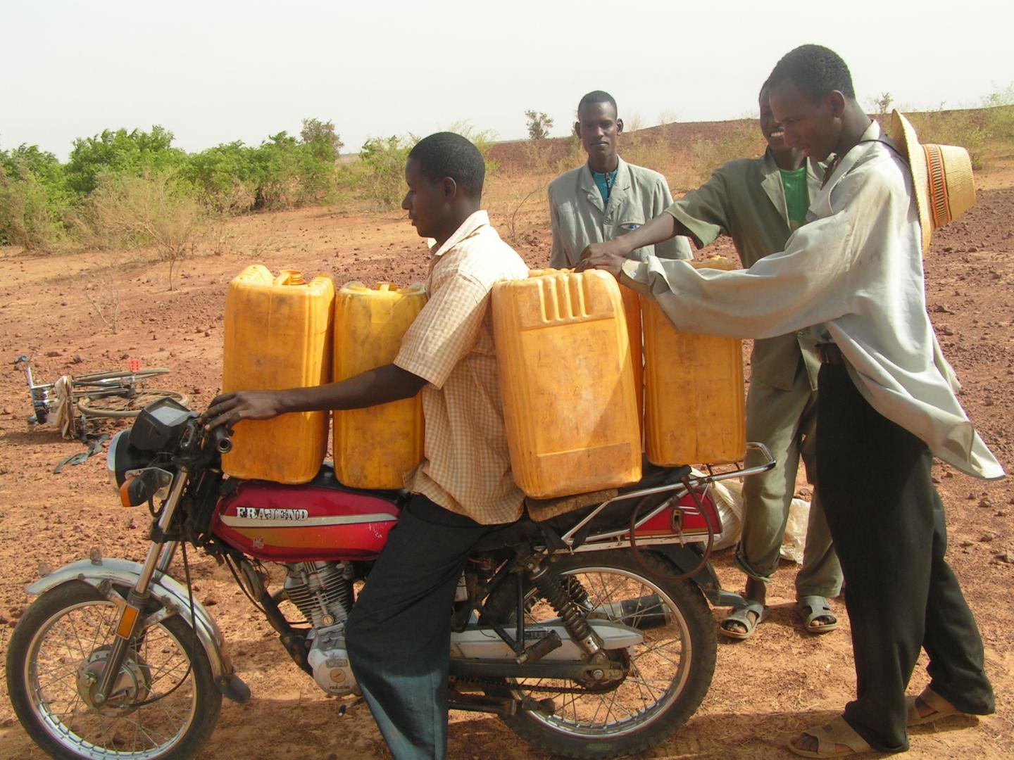 Driver sitting among cans that men are loading onto a motorcycle.