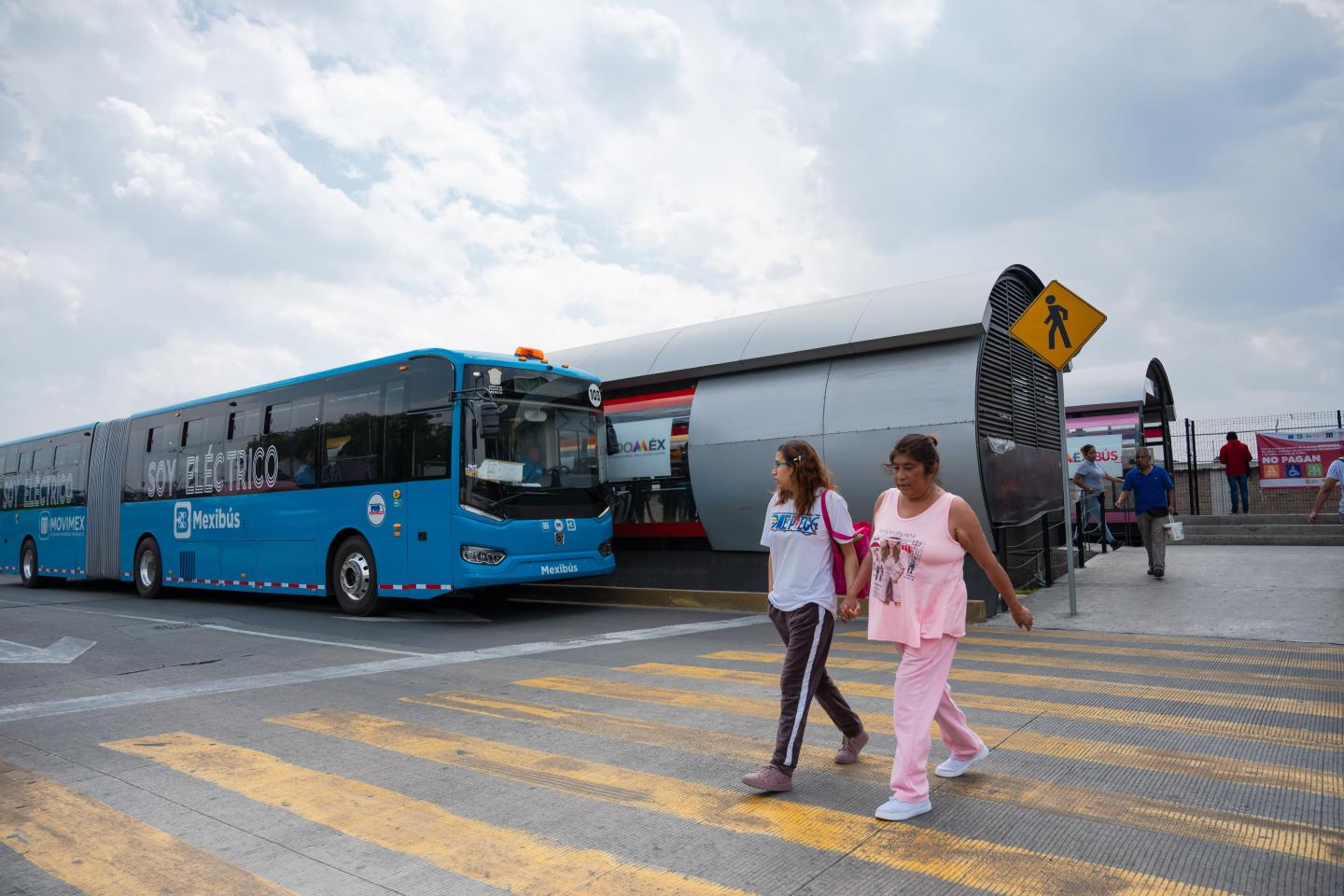 Dos personas cruzan una calle junto a la estación de autobuses rápidos.