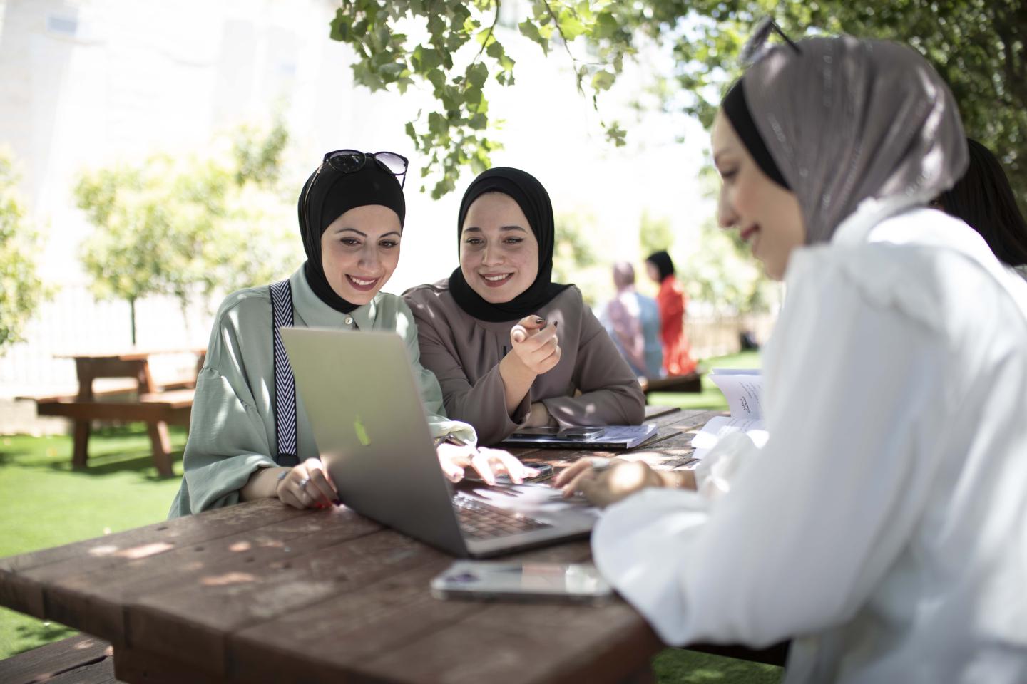 Studentinnen sitzen an einem Tisch zusammen um einem Laptop.