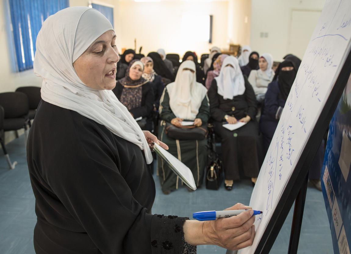 A woman writing on a flip chart, with many other women watching.