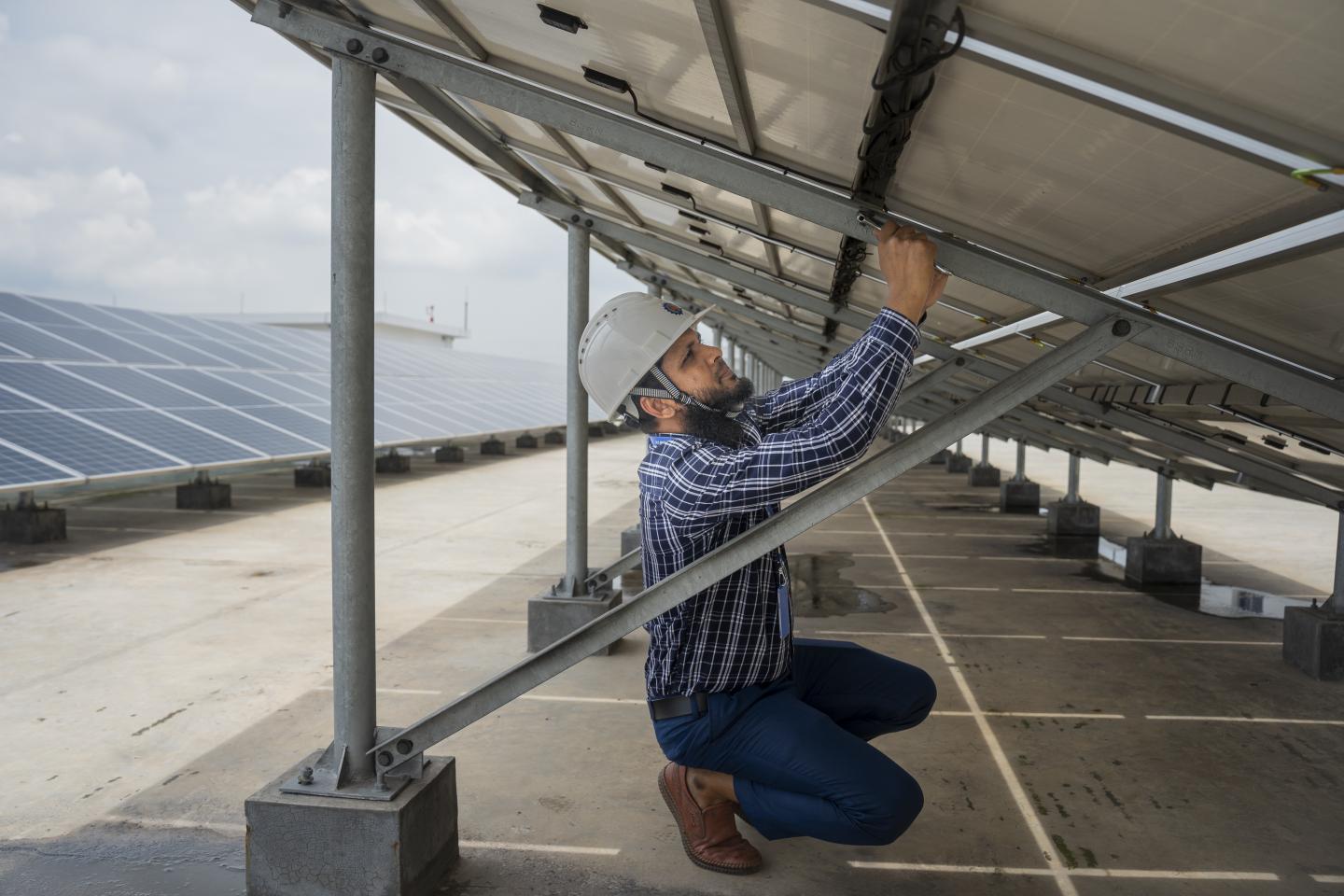 A man in a safety helmet works on a solar panel in a solar park.
