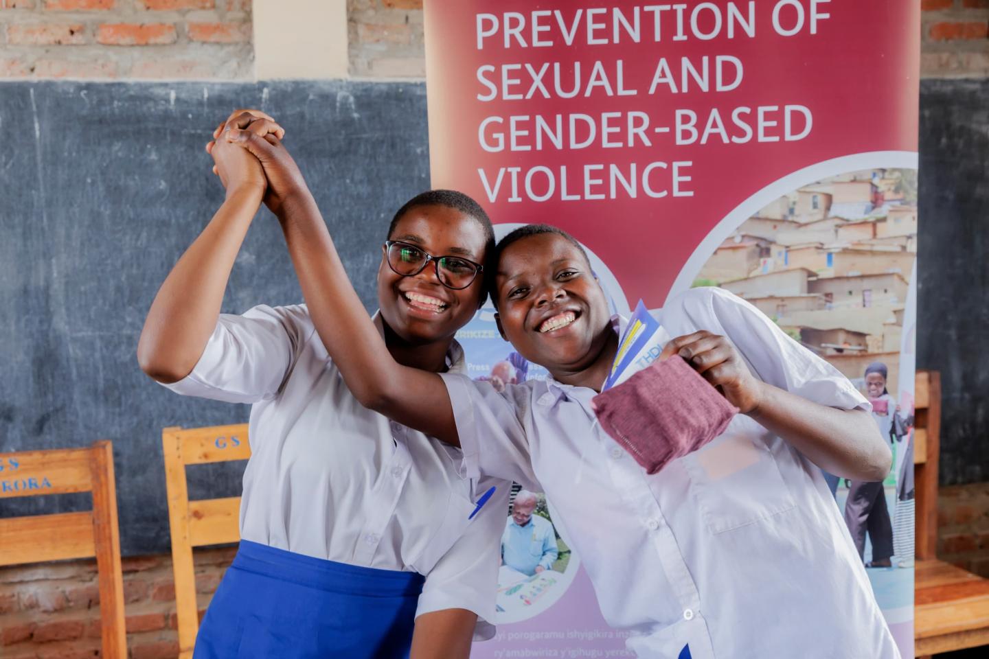 Zwei Mädchen lächeln und stehen vor einem Plakat für einen Workshop zur Prävention von Gewalt.