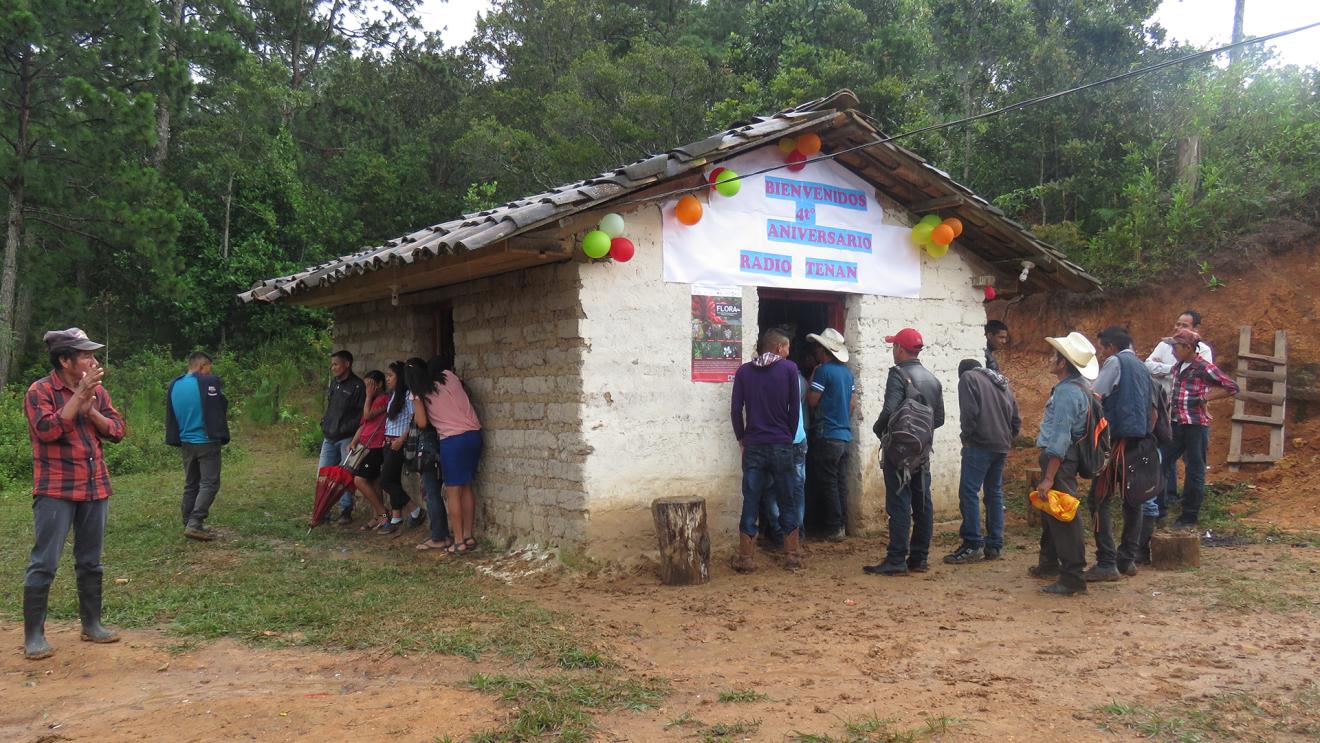 A group of people celebrate the fourth anniversary of a radio station in front of a hut.