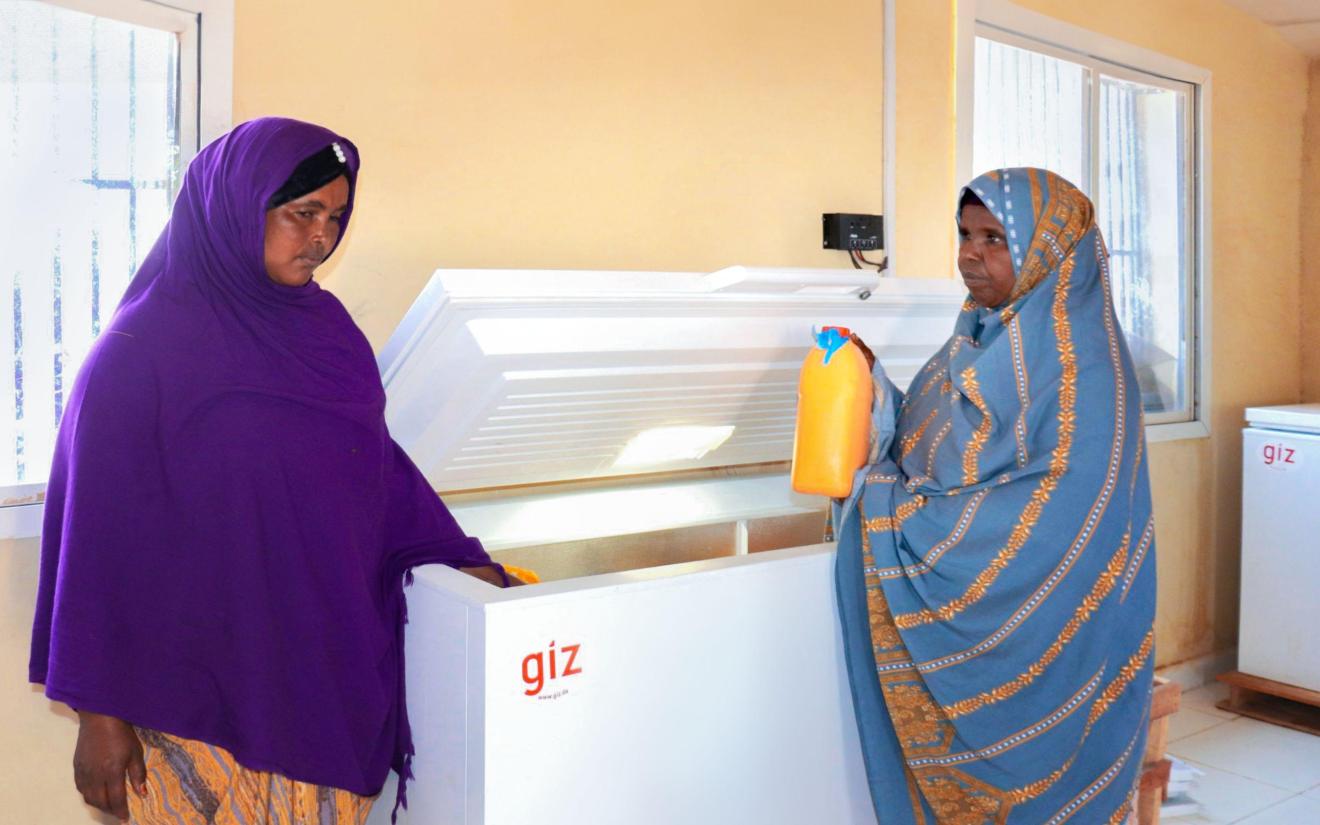 Two women are standing at a freezer cabinet, one of them is holding a milk container in her hand.