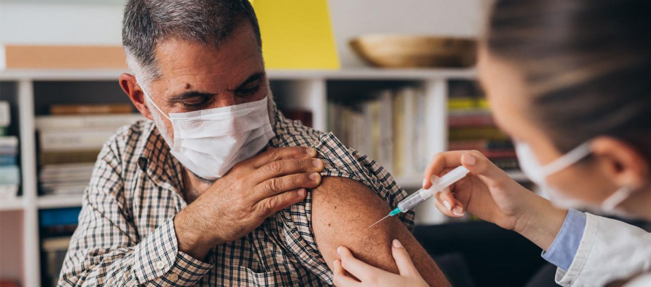A man receiving an injection in his upper arm from a second person.