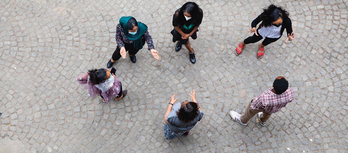 Aufnahme  äthiopischer junger Frauen und Mädchen sowie einem Mann von oben, die lebhaft miteinander diskutieren und auf einem gepflasterten Untergrund stehen. Die Kleidung der Personen variiert, mit sichtbaren Details wie einem Schal und unterschiedlichen Mustern auf den Oberteilen.