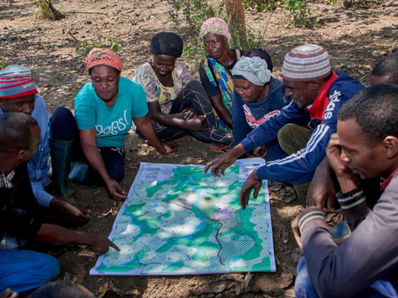 Viele Menschen sitzen auf dem Boden um eine Karte herum