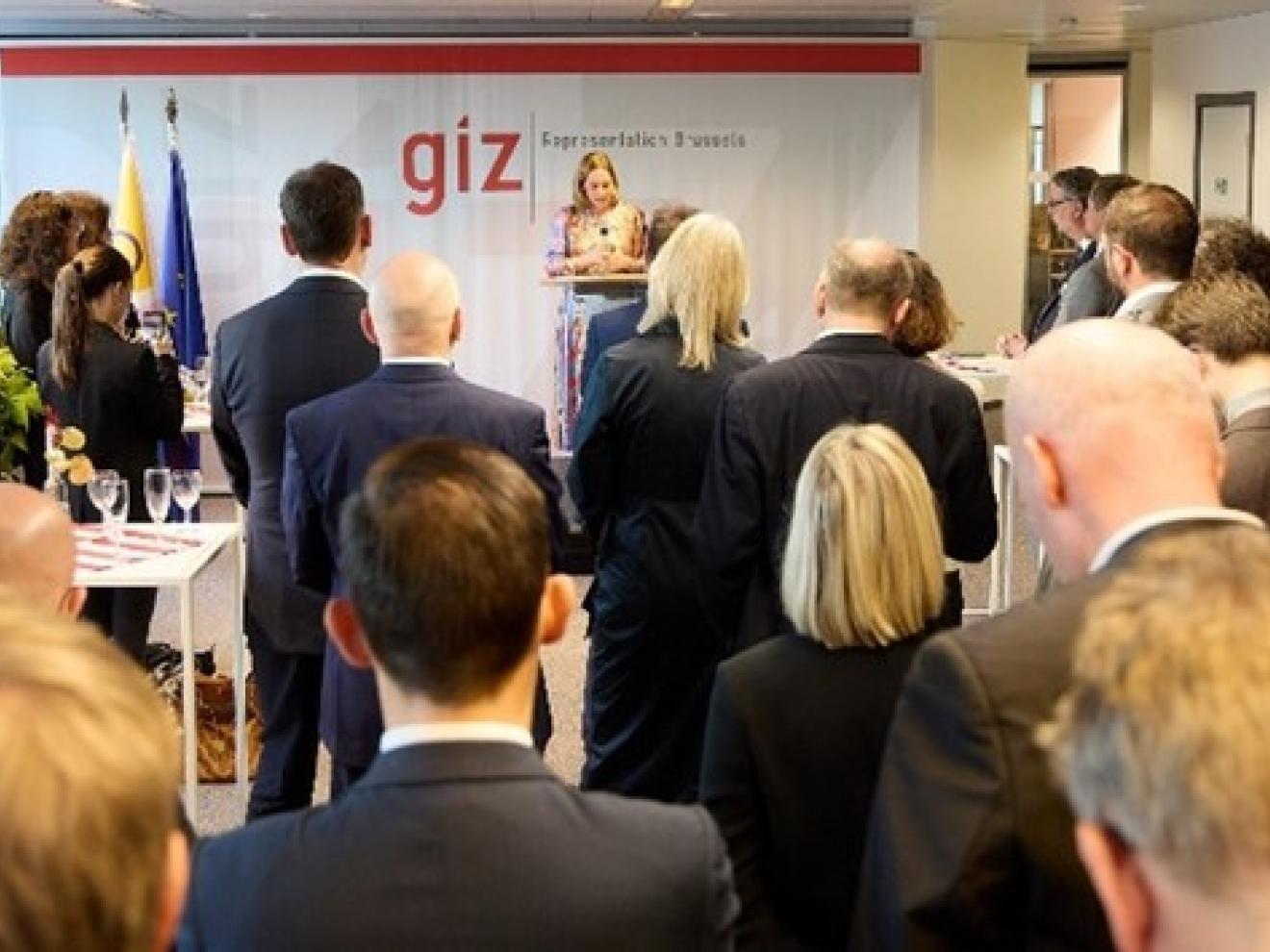 Viele Personen stehen in einem Raum und hören vorne einer Person zu