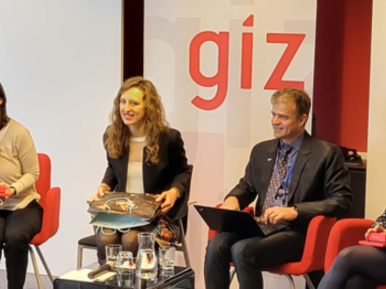 Mehrere Personen sitzen auf roten Stühlen in einem halb Kreis