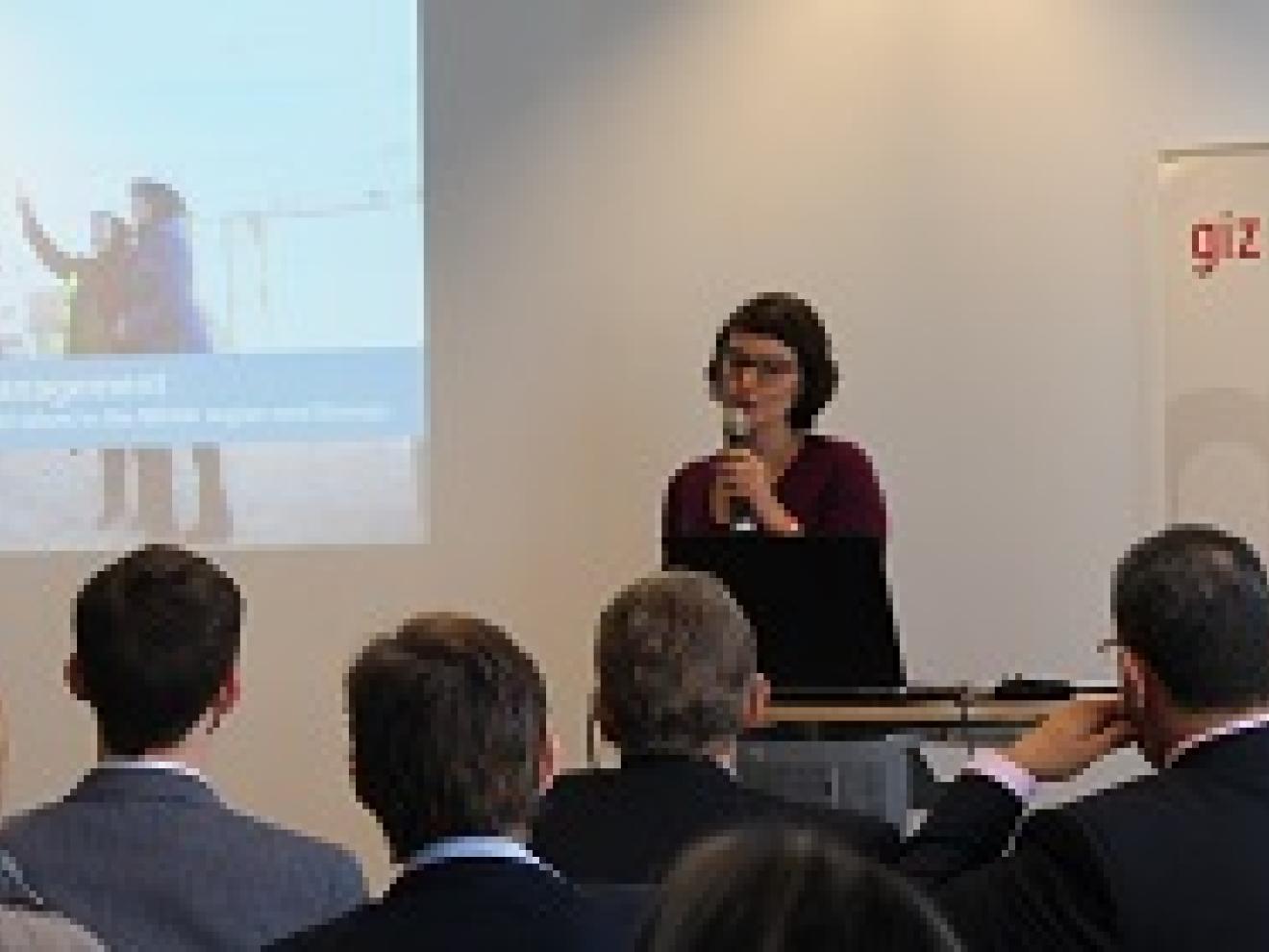 Person steht auf einer Bühne mit einem Mikrofon in der Hand vor Publikum