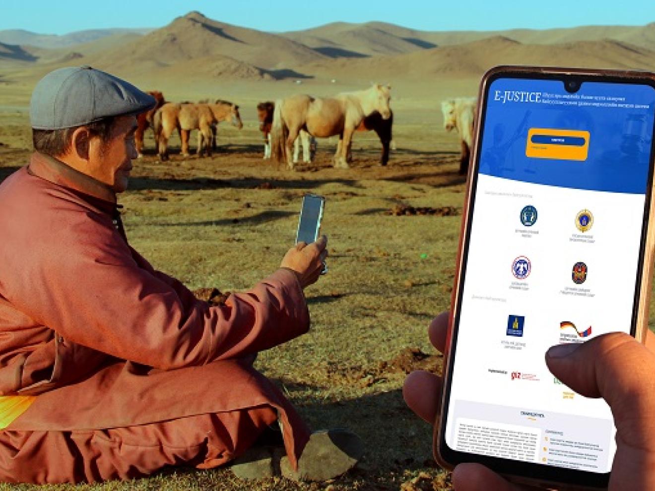 Ein Mann sitzt in der Steppe und hält ein Smartphone in der Hand.