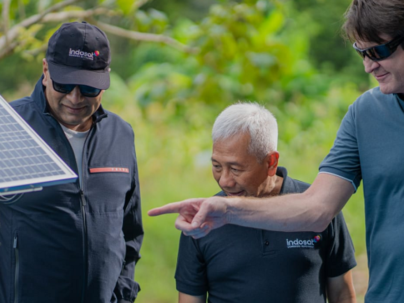 Drei Männer schauen auf ein Solarpanel, das in der Natur steht.