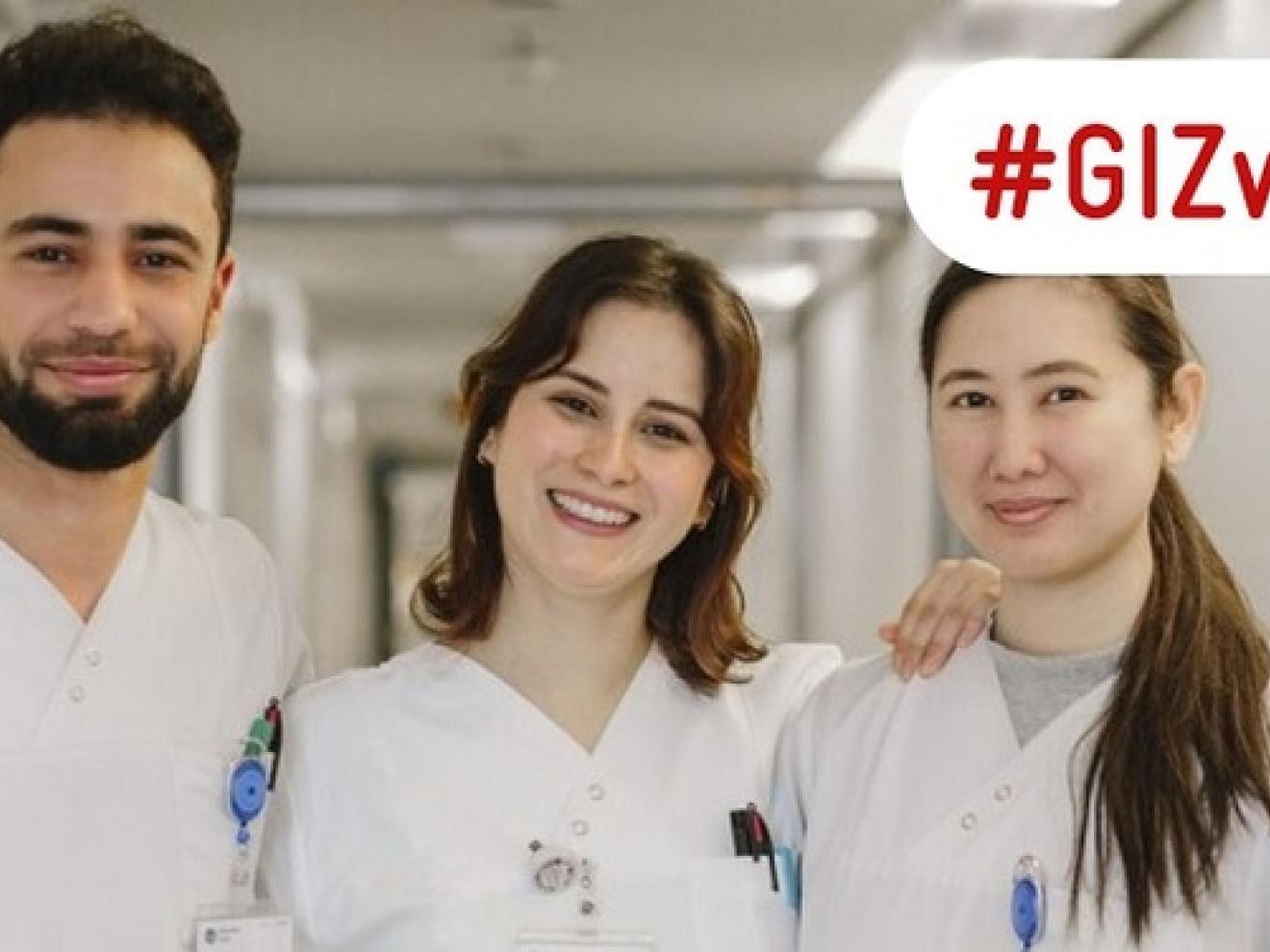Three qualified nurses stand in a hospital corridor smiling in the camera.