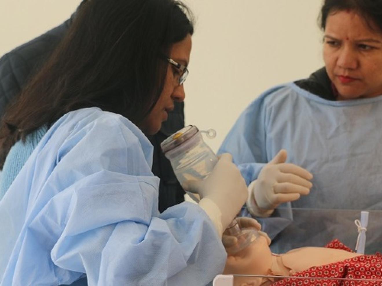 Zwei Frauen und ein Mann stehen um eine Simulationsbeatmung herum.