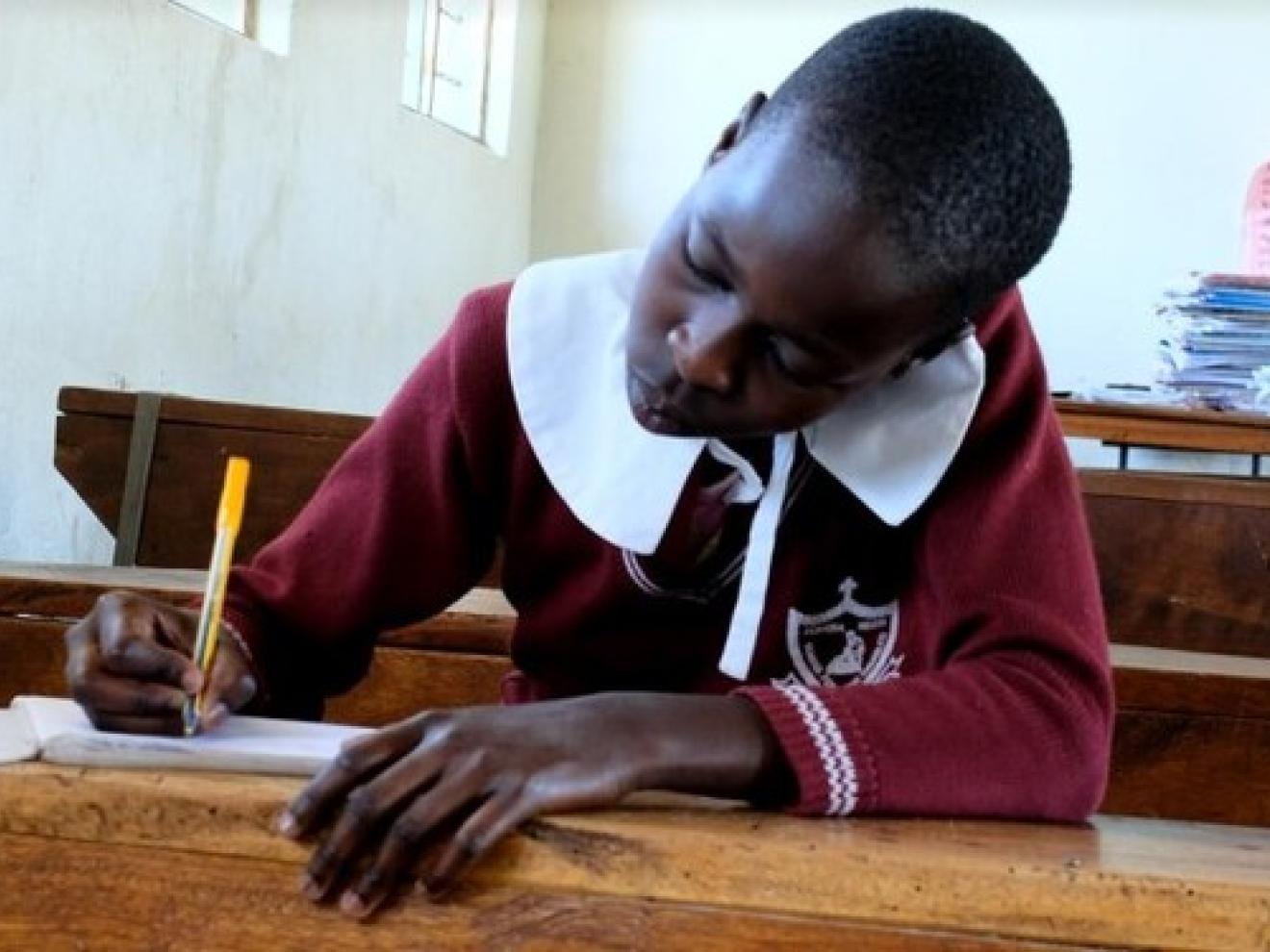 Ein Mädchen an einem Schulpult schreibt in ein Arbeitsheft.