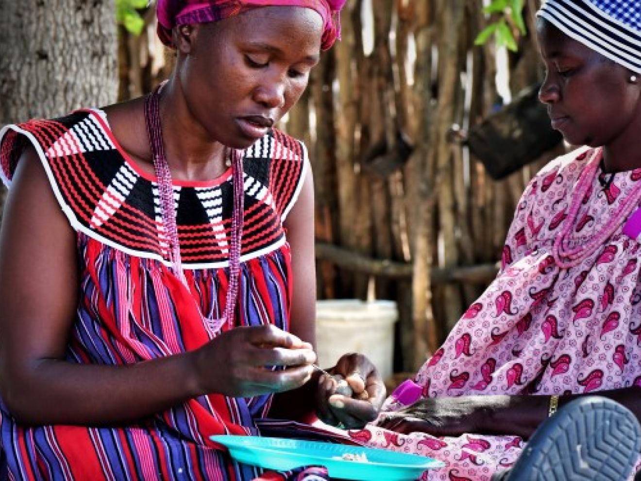 Two women sit together while one of them holds a marula nut in her hand.