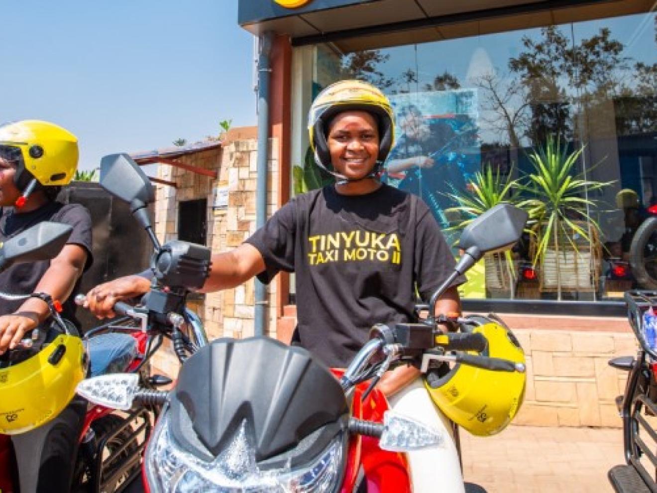 Women wearing helmets sit on motorcycles in front of a store