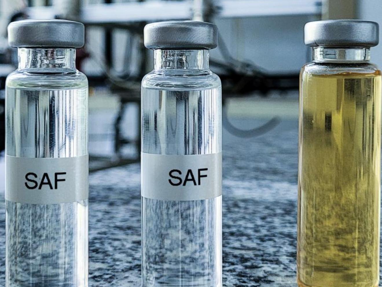 Mehrere Glasfläschchen mit Flüssigkeiten in verschiedenen Farben, beschriftet mit &quot;SAF&quot;, stehen in einer Reihe auf einer Granitplatte in einem Laborumfeld.