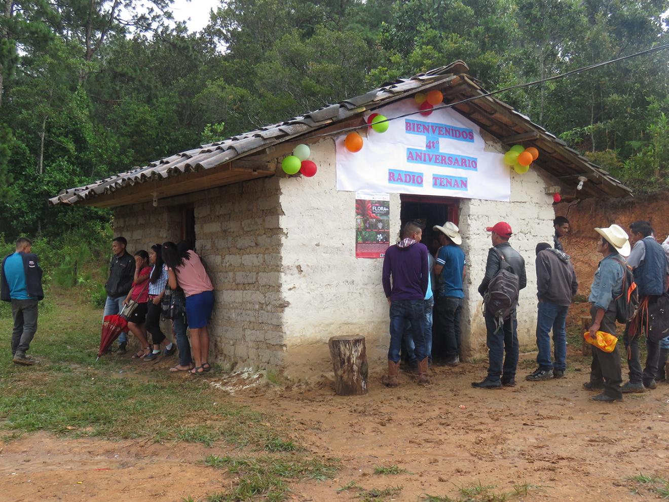 A group of people celebrate the fourth anniversary of a radio station in front of a hut.