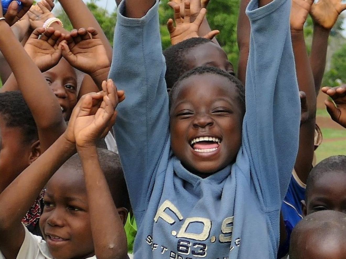 Eine Gruppe von Kindern streckt die Hände nach oben, alle lachen in die Kamera.