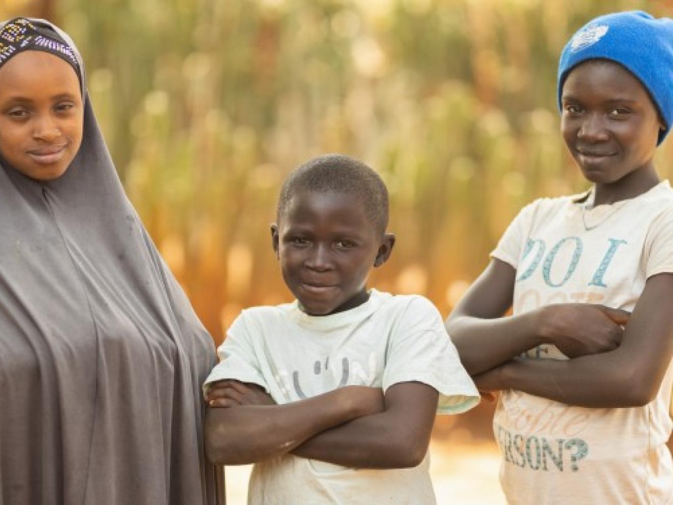 Three children are standing in front of a field.