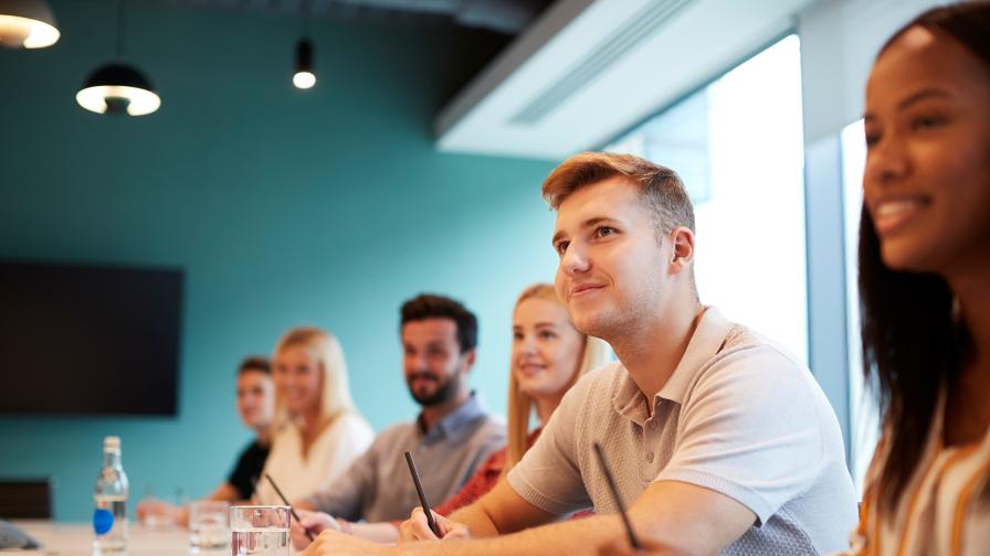 Junge Menschen sitzen an einem Tisch und hören einem Vortrag zu