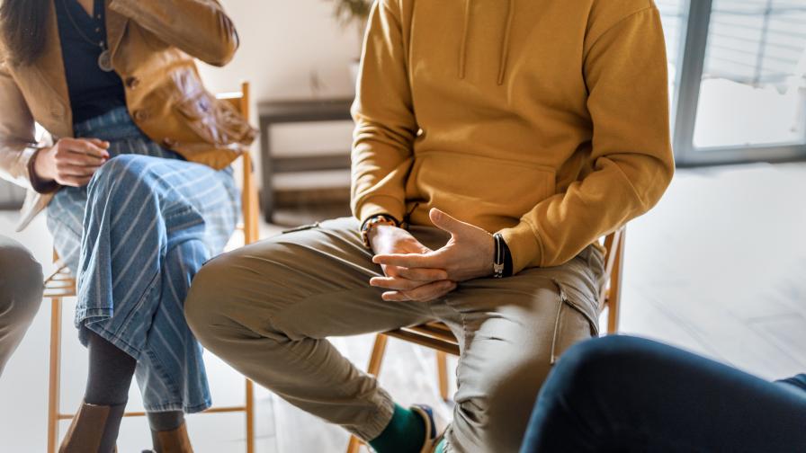 Teilweise sichtbare Menschen sitzen in einem Stuhlkreis in einer hellen Atmosphäre. Mit den Händen wird gestikuliert.