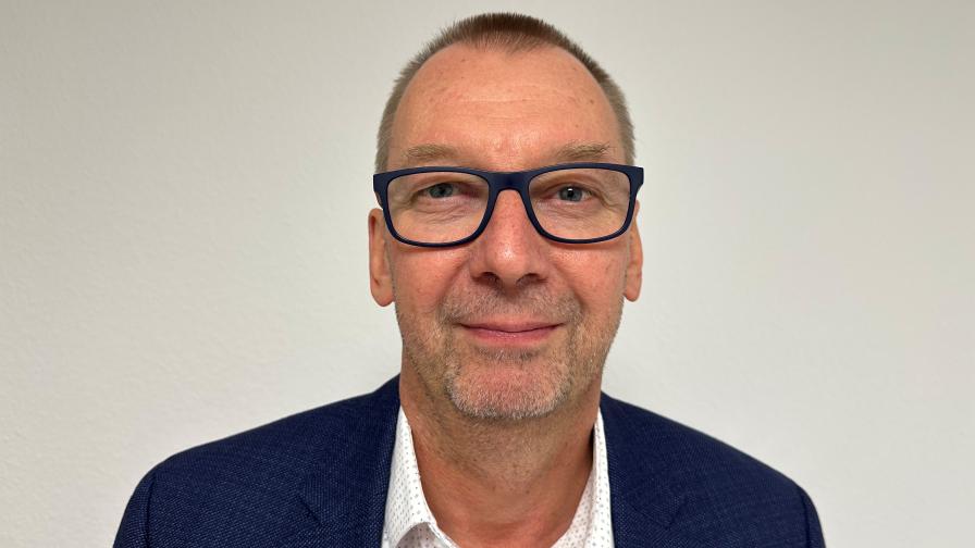 Photo of a smiling man with short, dark hair and glasses in front of a light-coloured background