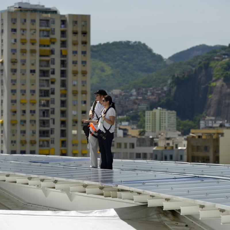 Zwei Menschen stehen neben PV-Paneelen auf dem Dach des Fußballstadions Maracanã in Brasilien. 