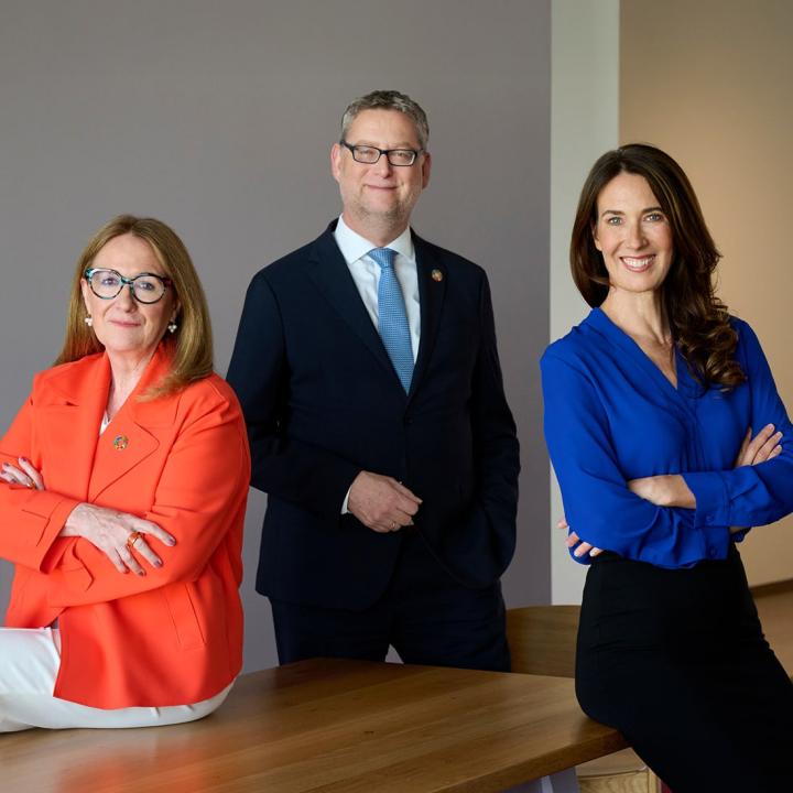 Drei Personen in professioneller Kleidung, zwei davon Frauen, in der Mitte ein Mann. 