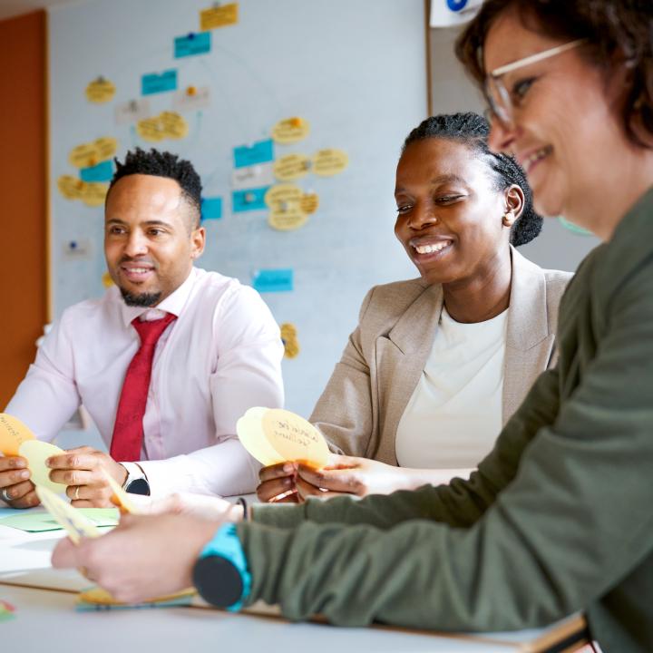 Two women and a man sit at a table, each holding some index cards.