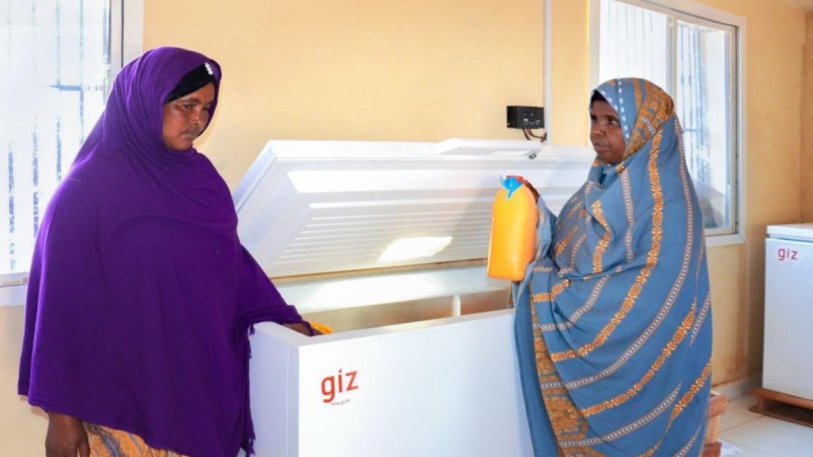 Zwei Frauen stehen an einer Tiefkühltrauhe, eine hält einen Milchbehälter in der Hand.