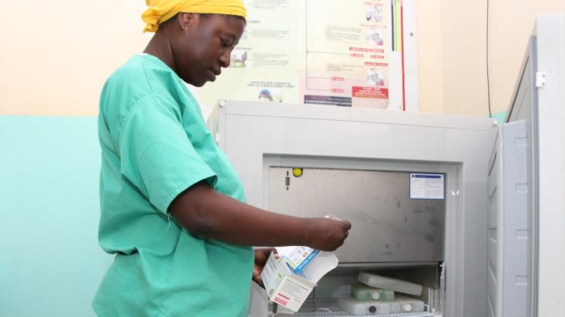 Eine Frau steht vor einem offenen Kühlschrank und legt Medikamente hinein. Sie trägt medizinische Berufskleidung.