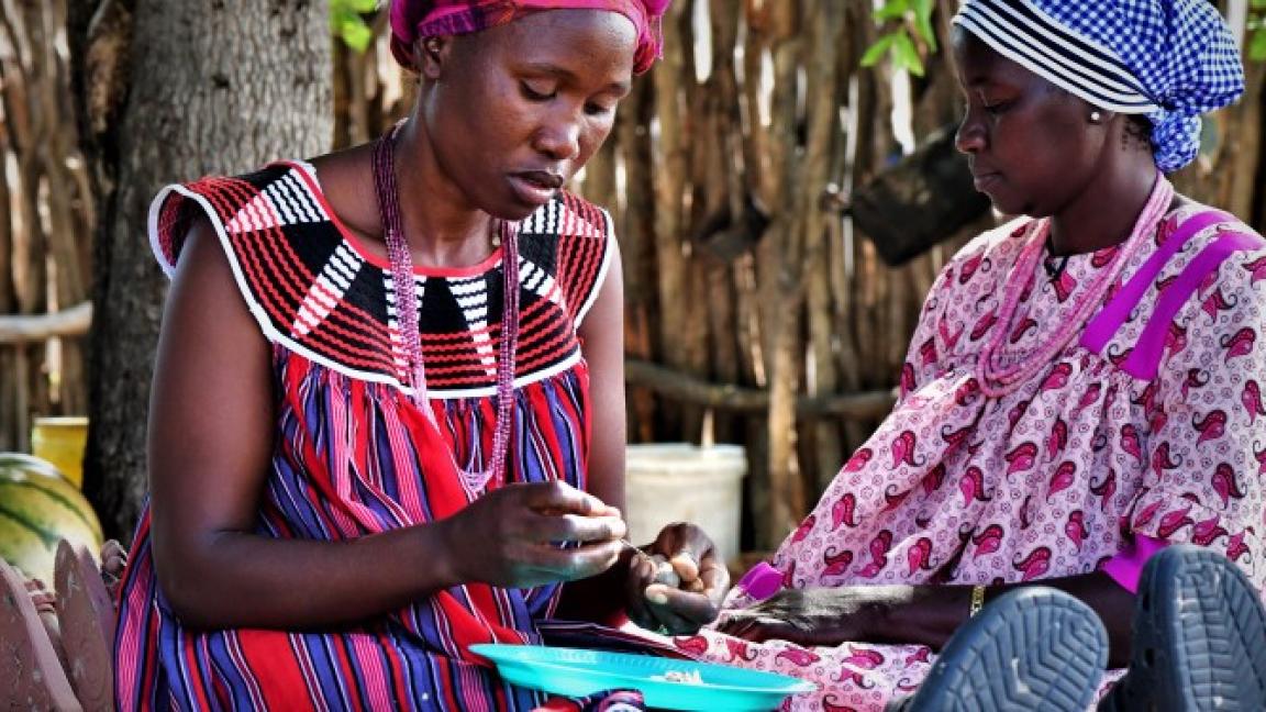 Two women sit together while one of them holds a marula nut in her hand.