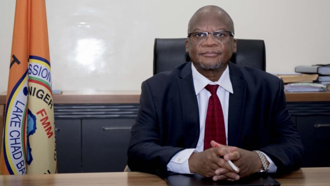 A man (Mamman Nuhu) sits at a desk and looks seriously into the camera.
