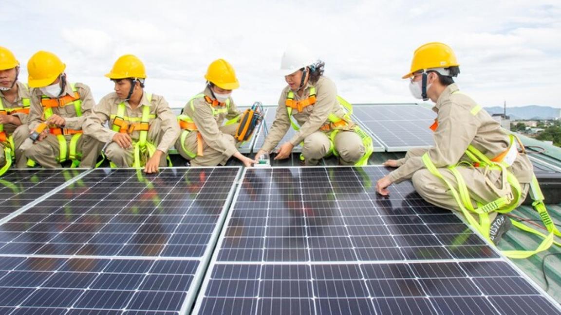 Young people in working gear are installing solar panels on a roof.