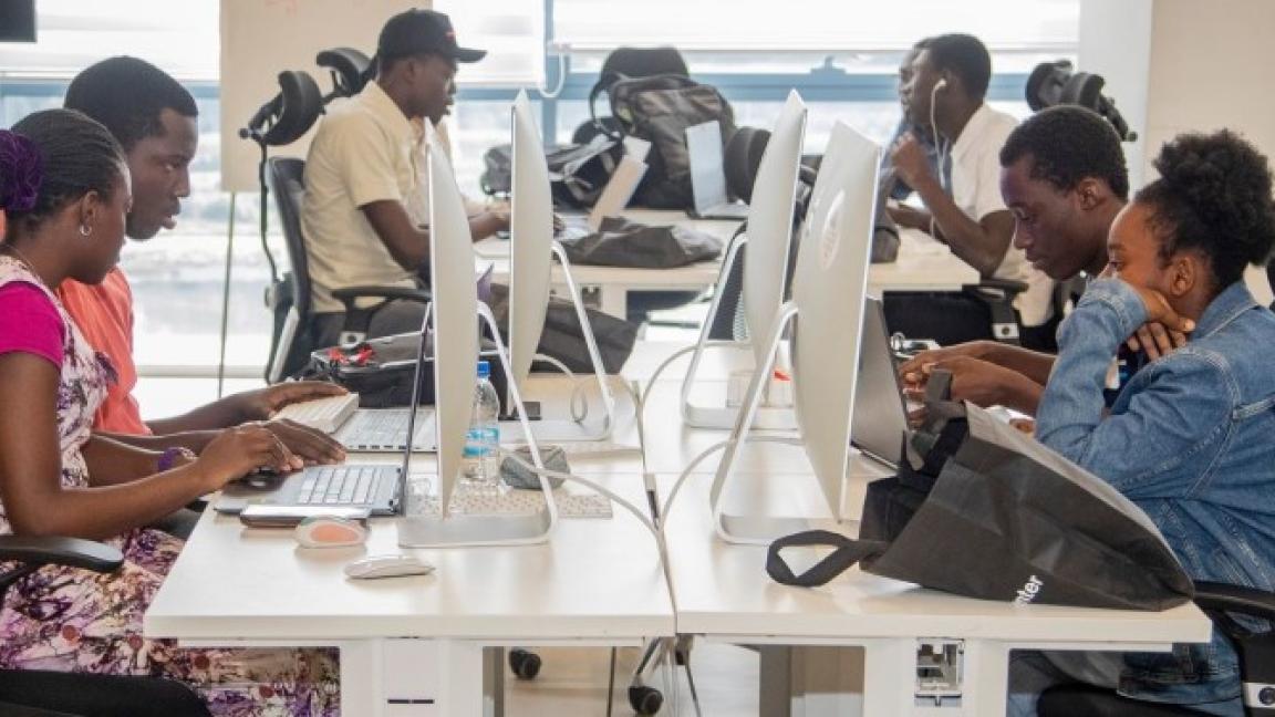 In einem Orange Digital Center sitzen sieben junge Menschen konzentriert vor Computerbildschirmen.