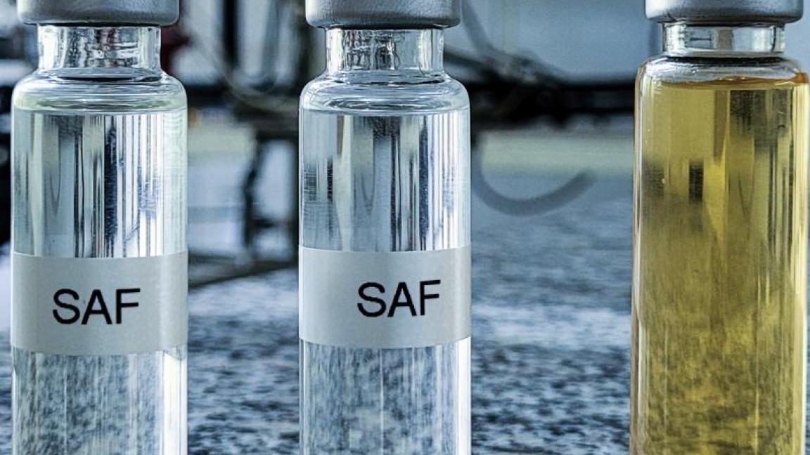 Mehrere Glasfläschchen mit Flüssigkeiten in verschiedenen Farben, beschriftet mit &quot;SAF&quot;, stehen in einer Reihe auf einer Granitplatte in einem Laborumfeld.