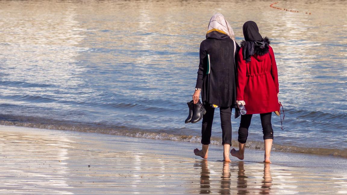 Two women walking on the beach with their backs to the viewer