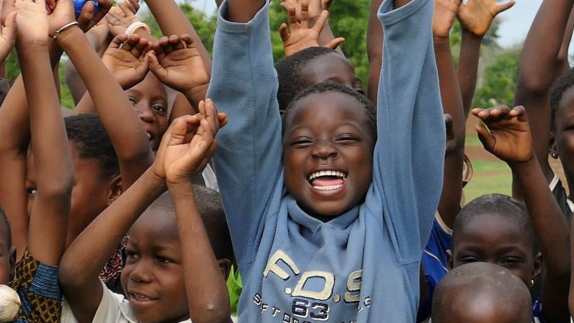 Eine Gruppe von Kindern streckt die Hände nach oben, alle lachen in die Kamera.