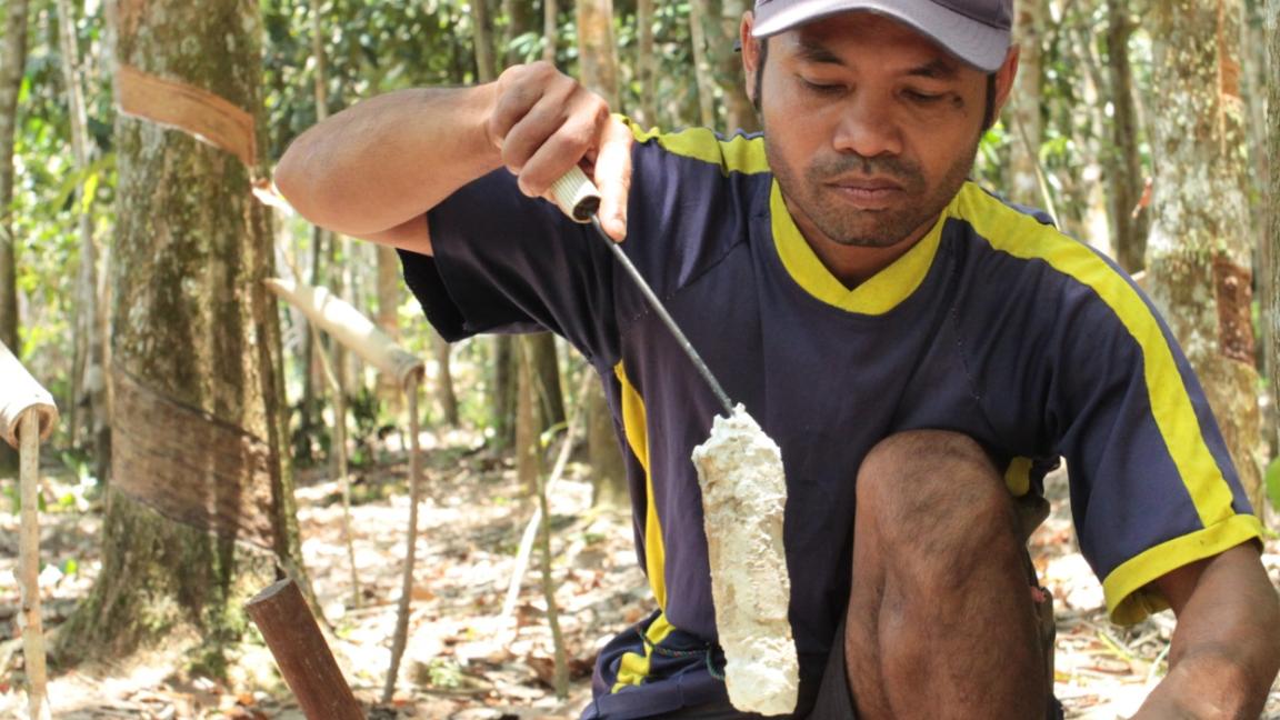 Zwei Männer mit weißen Bauhelmen halten eine Karte in der Hand, einer zeigt auf drei Windräder im Hintergrund.