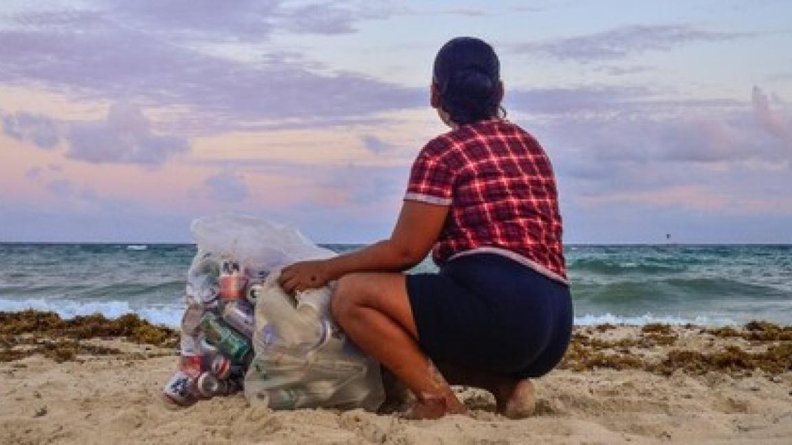 A woman sits on a beach in Mexico next to two full bags of trash she collected earlier.