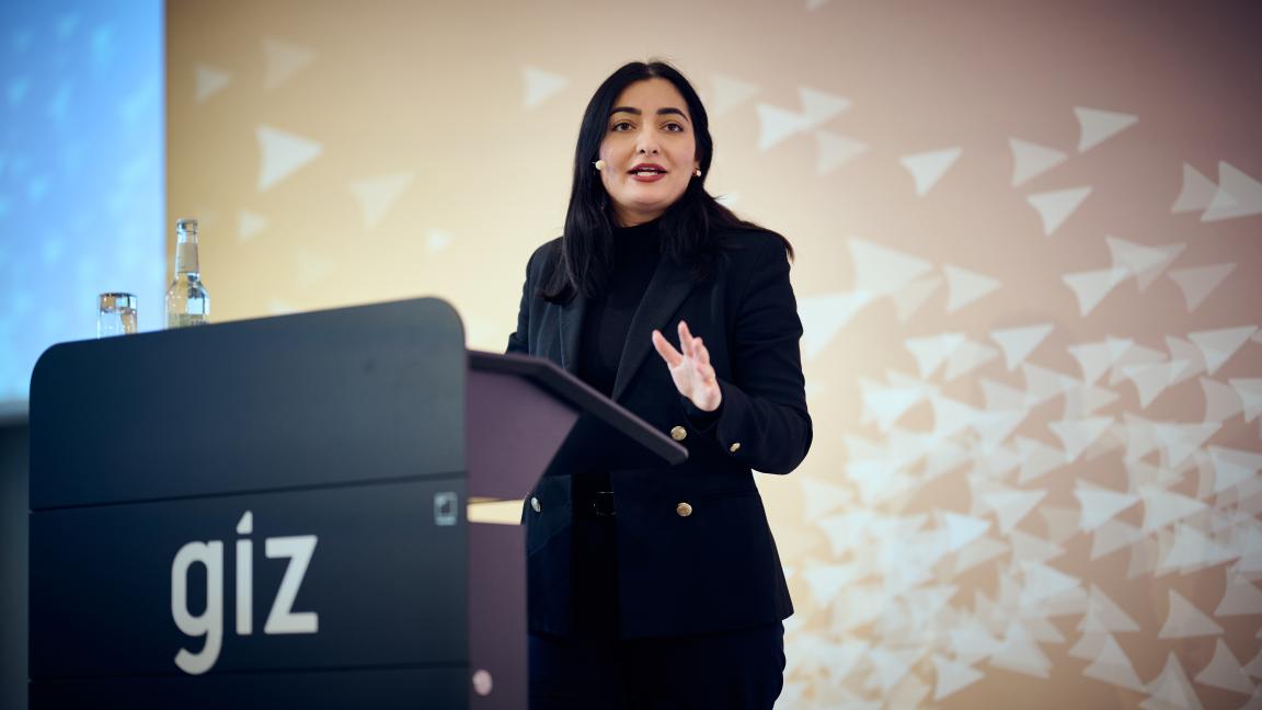 A woman with dark hair is standing behind a lectern.