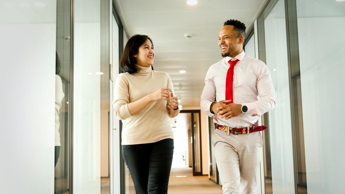 Zwei Personen gehen durch einen Büroflur und unterhalten sich.