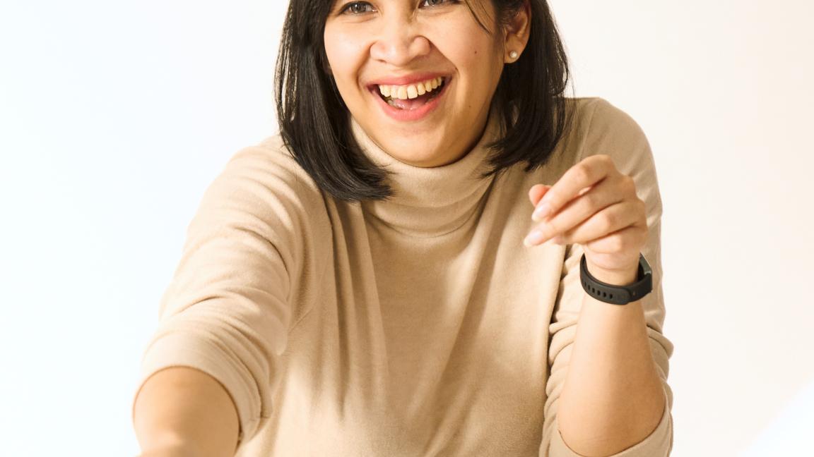 Person sitzt an einem Tisch, lächelt und reicht eine Haftnotiz; auf dem Tisch liegen Marker und weitere Haftnotizen.