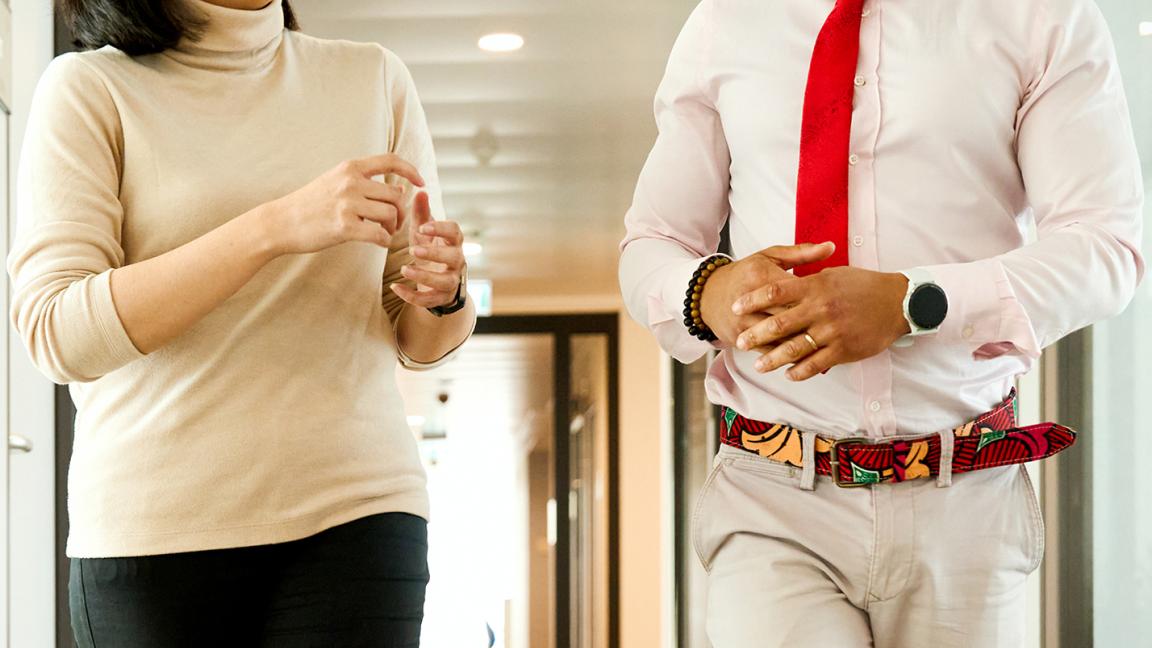 Zwei Personen gehen durch einen Büroflur und unterhalten sich.